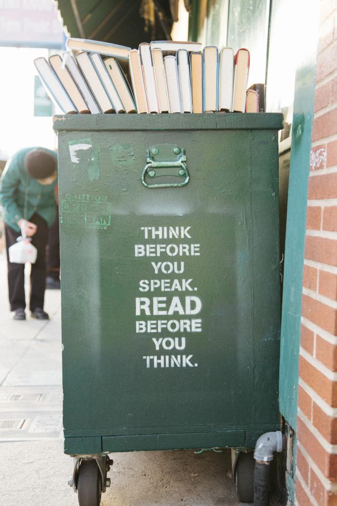 Books stacked on a rolling cart with the phrase 'Think Before you speak. Read before you think.' painted on the side.