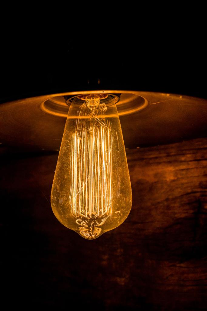 Edison style light bulb lit and glowing orange against a dark wood background.